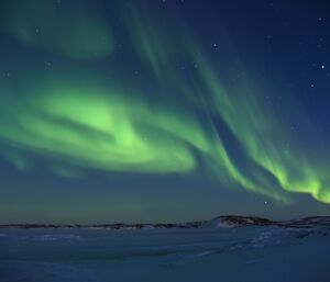 Green aurora hanging in a thread and curled above the pre-dawn sky with snow covered rocky terrain in foreground