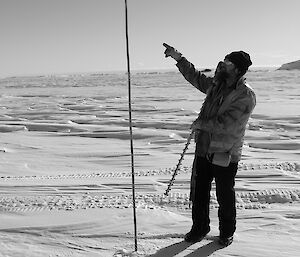 Expeditioner pointing in side profile to a bamboo cane set into the sea ice