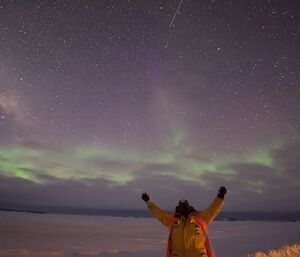 Expeditioner standing with arms outstretched beneath the night sky