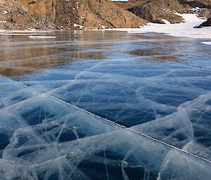 Blue frozen lake ice with thin white frosted ice lines running through it