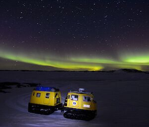 Yellow tracked vehicle illuminated against night sky with a green aurora hanging in the sky