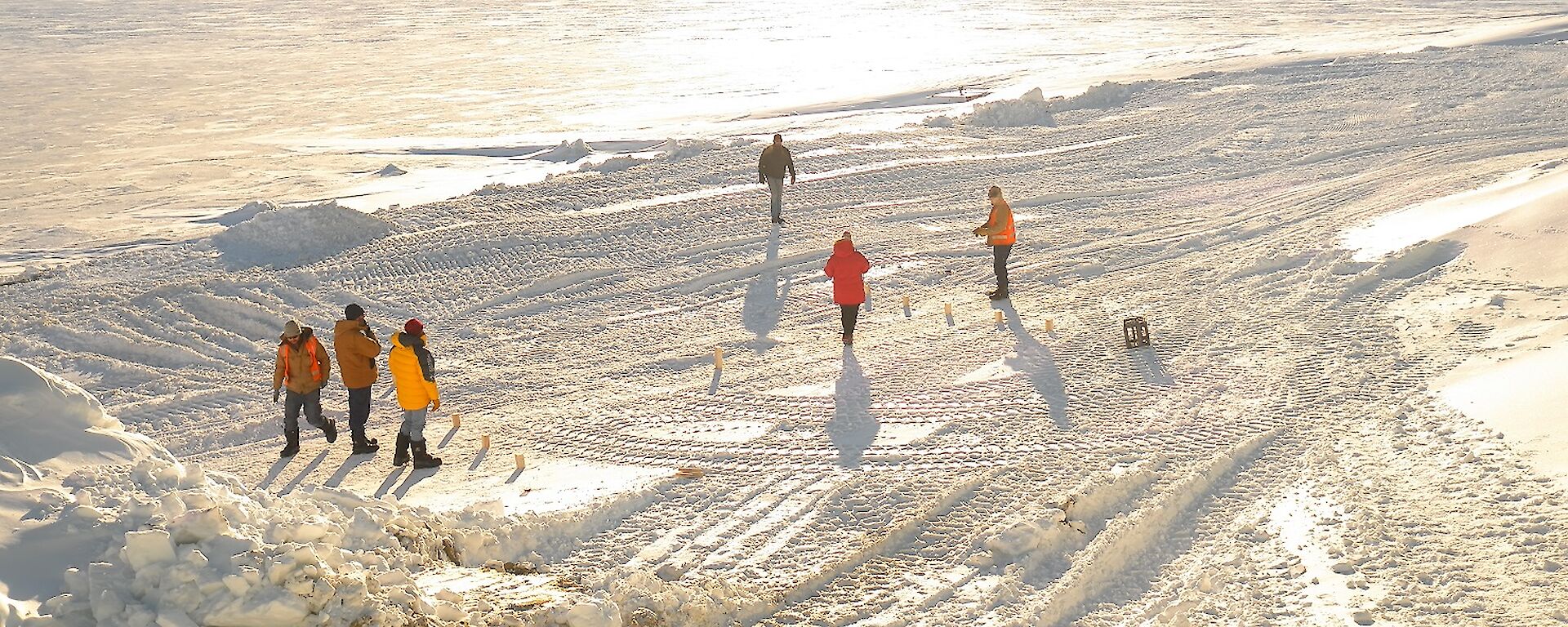 Expeditioners stand at either end of a rectangular pitch with sea ice and ice bergs in background