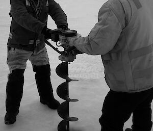 Two expeditioners drilling through sea ice with an auger