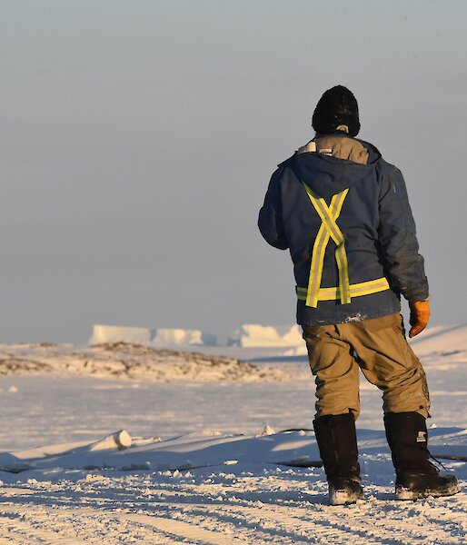 Expeditioner standing back to camera with sea ice in background