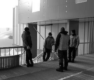 Four expeditioners facing towards camera in front of living quarters