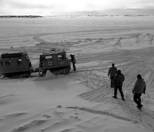 Four expeditioners make their way towards a hagg with sea ice in background