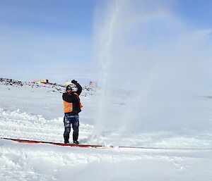 Expeditioner standing beside a water hose spraying water, pretending to bathe