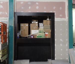 Plaster wall beyond a concrete floor with cardboard boxes piled high in a cavity