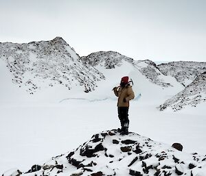 Expeditioner standing on a rocky outcrop with sea ice and snow covered hills in background