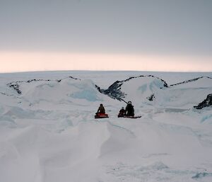 Three expeditioners moving away from camera between sea ice tide cracks driving quad bikes