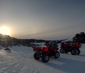 Quad bikes parked up with a sun setting over snow covered landscape on left hand side