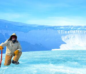 Expeditioner crouching with an ice axe in front of a natural ice amphitheater