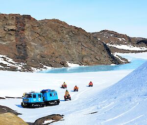 A blue tracked vehicle and several quad bikes parked beneath a large wind scour