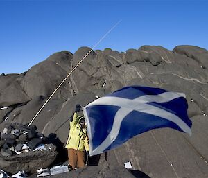 Expeditioner holding the scottish national flag beneath a rocky outcrop
