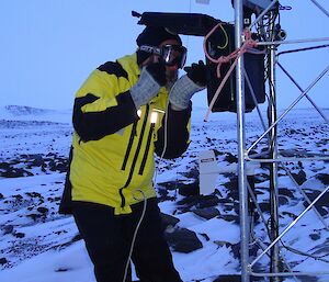 Expeditioner holding a torch stands beside a metal scaffold tower with snow covered terrain in background