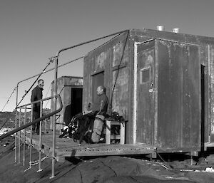 Two expeditioners outside on the sun deck of a hut with rocky terrain in the background