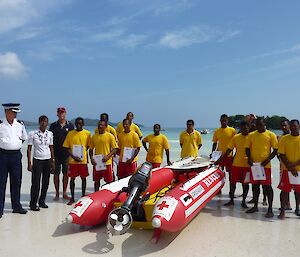 A gathering of local young men dressed in red shorts and t-shirts around a rubber dinghy with tropical island and water in background.