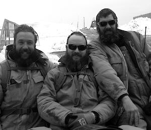 Three expeditioners crowded around a quad vehicle facing camera smiling