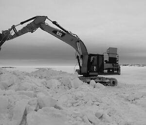 Expeditioner in an excavator with claw extending out shoveling snow