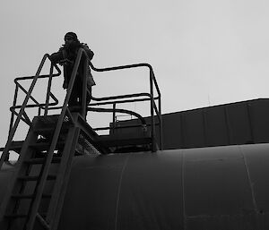 Expeditioners silhouetted on the top of a ladder next to a fuel tank