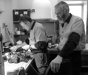 Two expeditioners hunched over a workstation with fibre optic cabling across a workbench