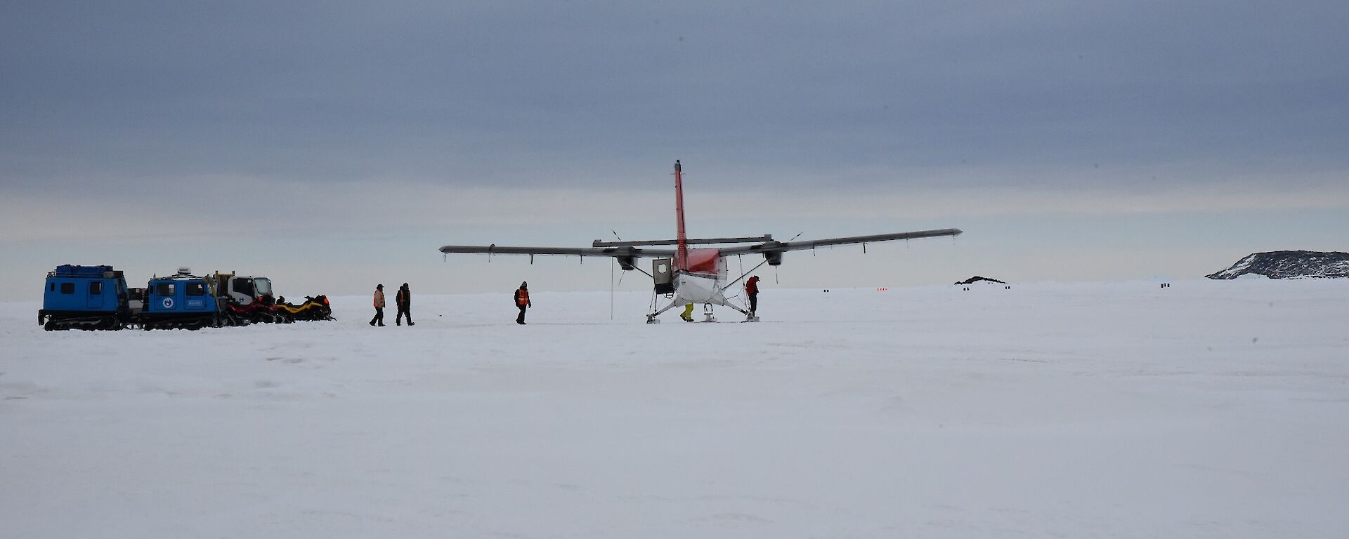 Vehicles parked close to an aeroplane with individuals walking around the aircraft