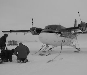 Three aircrew secure their aircraft as winds whip up around the aeroplane and tracked vehicle with station in background