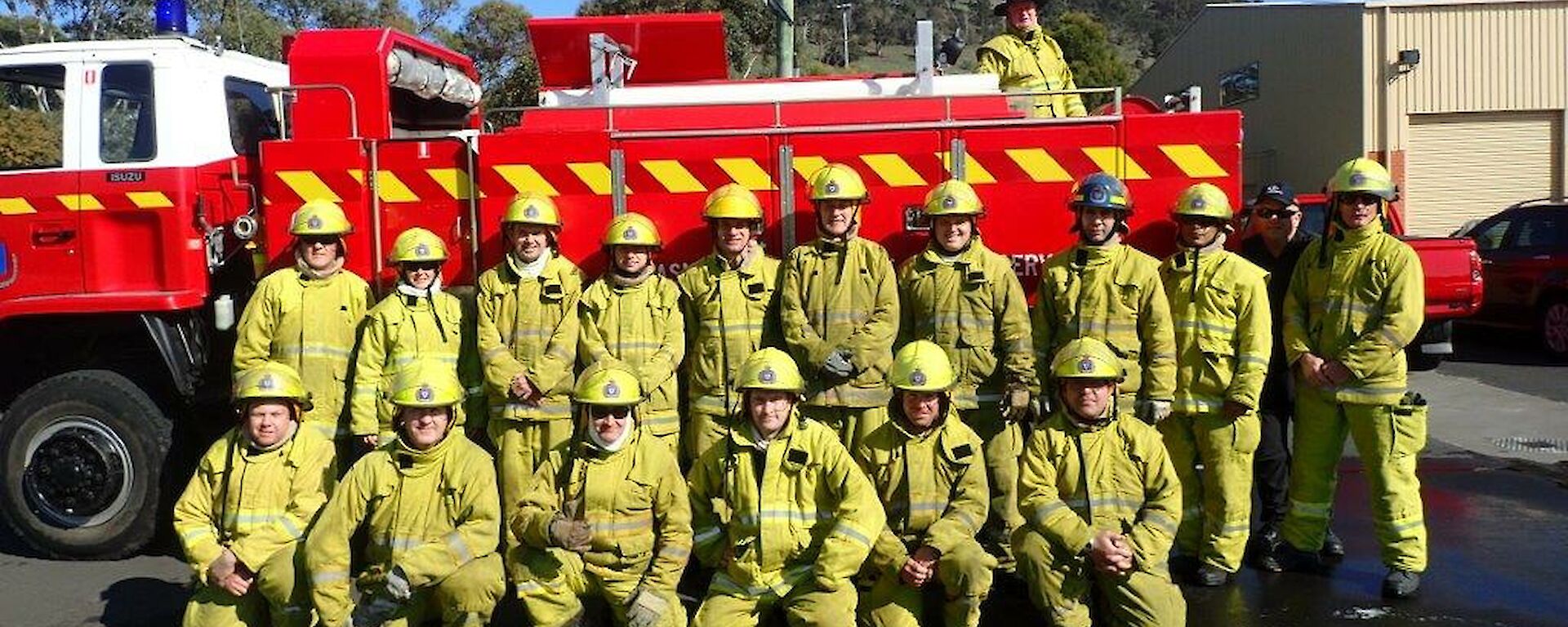 Large group of people in fire fighting gear pose together in front of a fire truck