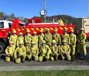 Large group of people in fire fighting gear pose together in front of a fire truck