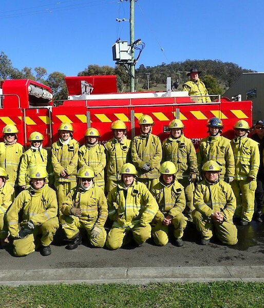 Large group of people in fire fighting gear pose together in front of a fire truck