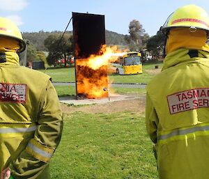 Expeditioners look at a fire taking hold of a standing rectangular structure during training