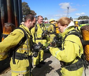 A female expeditioner in fire fighting gear helps a male expeditioner with some equipment