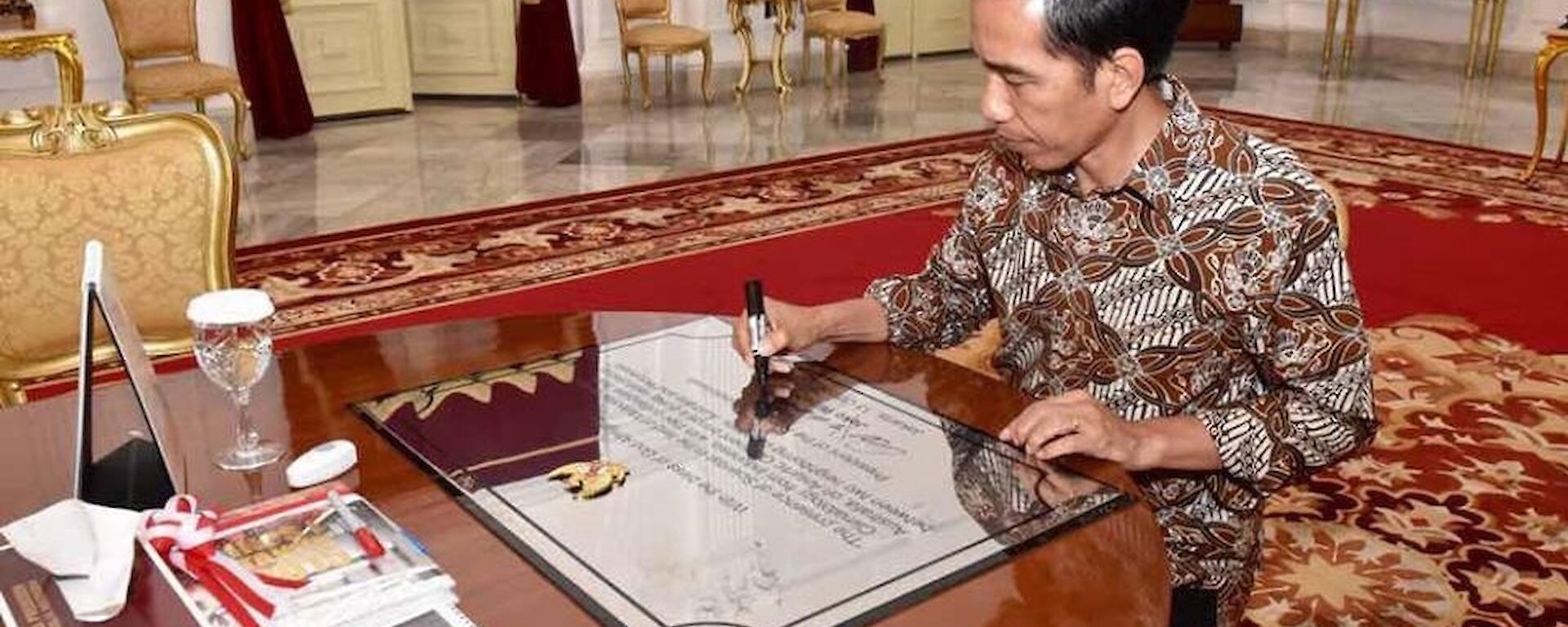 The Indonesian President siting at a desk signing a plaque