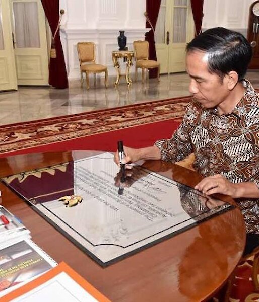 The Indonesian President siting at a desk signing a plaque