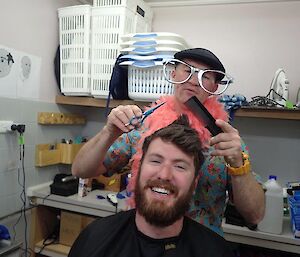 An expeditioner getting a haircut from the chef who dressed in a French custume
