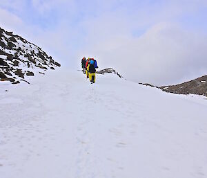 Expeditioners walking up a snow incline on the side of a steep hill