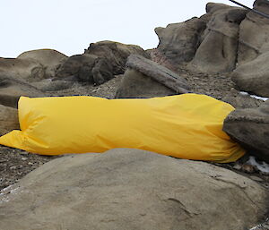 An expeditioner asleep in his sleeping bag out on the rocks in the open air