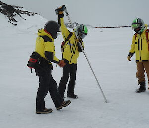 Three expeditioners drilling the sea ice to ascertain the depth