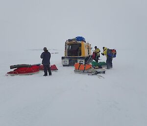 Three scientists removing equipment from a haggland in snowing conditions on the ice
