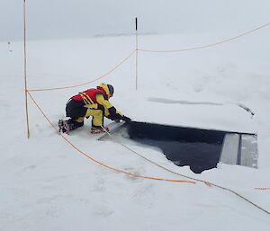 A scientist removing a wooden cover from a pre-drilled hole in the ice