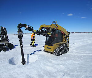 A Skidsteer machine drilling a large hole in the ice