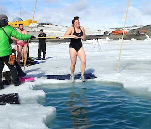 An expeditioner about to enter the water for a swim in an ice hole