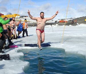 An expeditioner with his hands in the air stepping into freezing water