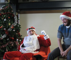Santa with an expeditioner sitting on a stoll next to him.