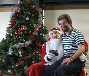 An expeditioner sitting on Santa’s knee getting a present