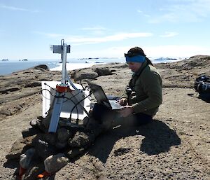A scientists sitting on a rock with a computer