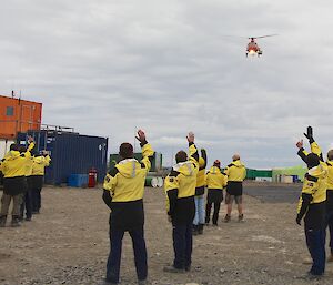 A helicopter flying over a number of expeditioners waving goodbye