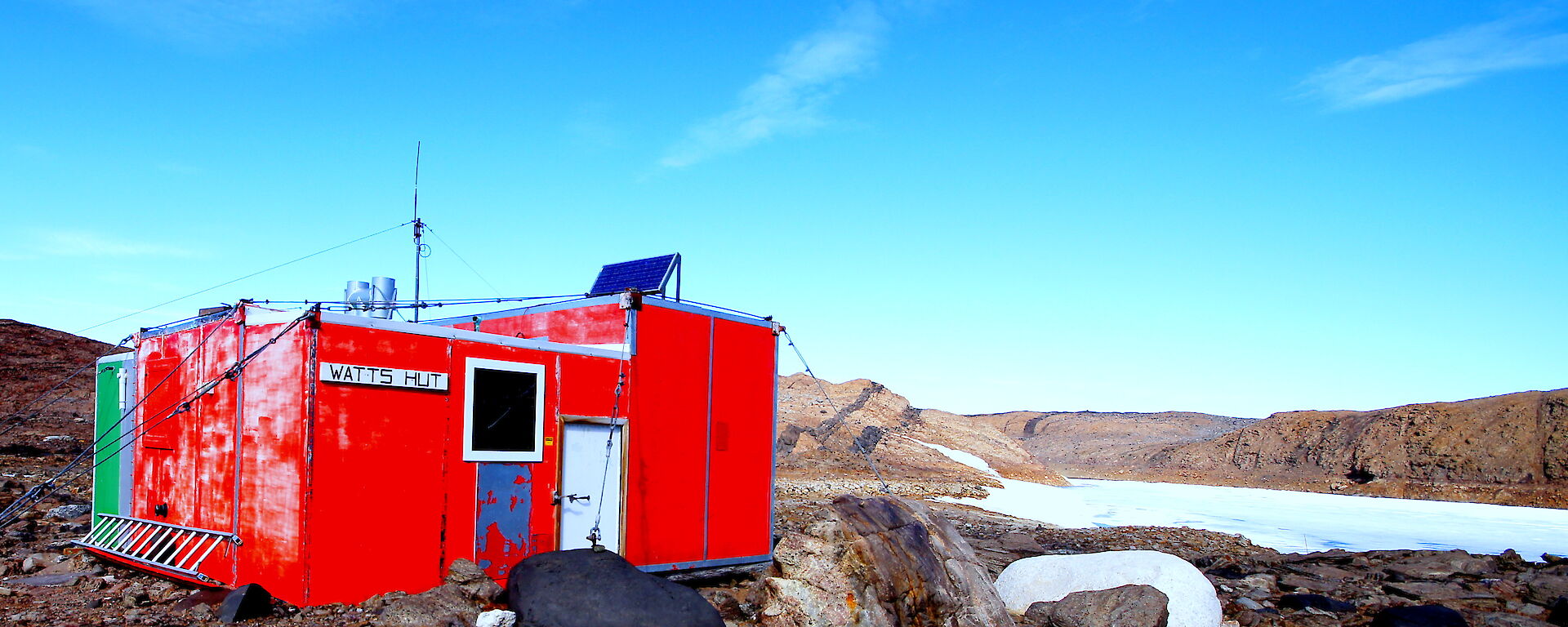 Watts hut against a vivid blue sky and rocky backdrop