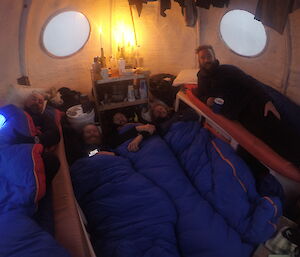 Five expeditioners preparing to go to sleep in their sleeping bags all squeezed inside Crooked Lake apple hut