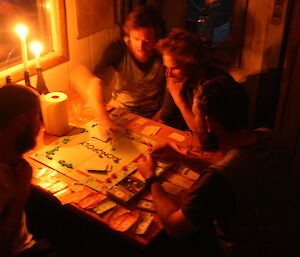 Scott McMillan, Bryce Daniels, Dan Mizza and Cam Lea playing Monopoly by candlelight at Brookes hut in the Vestfold Hills